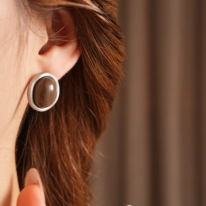 Close-up of brown oval resin earrings with silver metal trim worn by a model