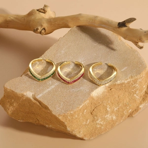 Three V-shaped gold rings with green, red and white crystals on a textured sandstone