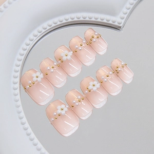 Pink cat eye press-on nails with pearl flowers and gold beads on a mirror tray