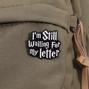 Close-up of black quote pin with I'm Still Waiting For My Letter on a canvas backpack