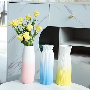 Modern gradient ceramic vases in pink, blue and yellow with roses on a white table