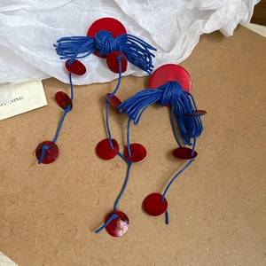 Detail of red circular stud earrings with blue wax rope tassels and small shell accents