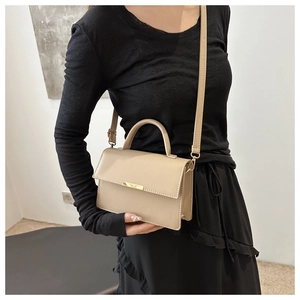 Detailed view of beige leather handbag featuring a gold metal bar and top handle