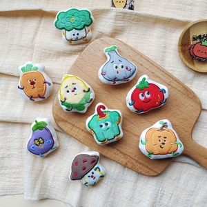 Nine cartoon vegetable plush brooches on a wooden board and beige wrinkled fabric