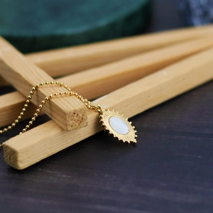 Bohemian gold beaded chain necklace featuring a geometric oval shell pendant on wood