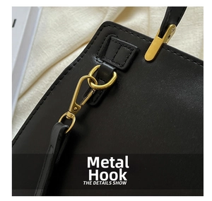 Detail of matte gold metal swivel hook and textured black leather strap of the bag