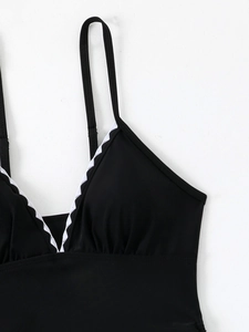 Detail of V-neck swimsuit with white scalloped trim and ruched black stretchy fabric