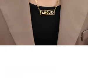 Gros plan d'un collier chaîne gourmette dorée avec pendentif AMOUR porté par un mannequin