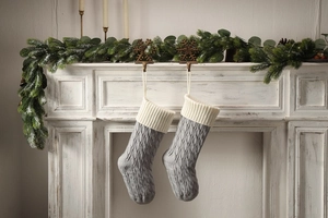 Close-up of grey knitted Christmas stockings with cable patterns on a white fireplace
