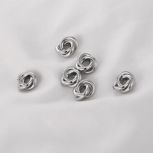 Primer plano de cinco cuentas de nudo plateadas para joyería DIY en tela blanca