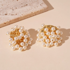 Close-up of elegant gold clustered pearl earrings on a textured stone background