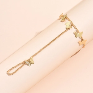 Detailed close-up of golden butterfly ring bracelet chain on a soft pink background