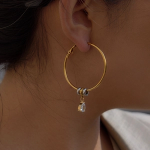 Nahaufnahme von goldenen Creolen mit Zirkonia-Tropfenanhänger an einem Frauenohr