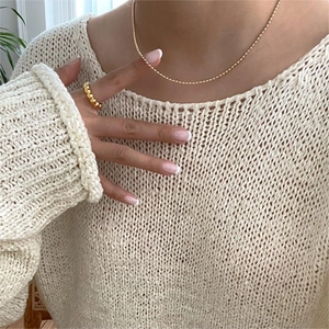 Close-up of gold beaded chain necklace and textured ring on a beige knit sweater background