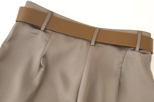 Detail of high-waist grey satin wide-leg trousers with matte brown belt accent