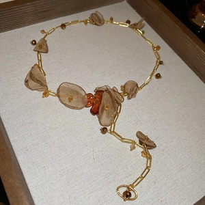 Detailed view of chiffon flower charms and crystal beads on a gold chain necklace