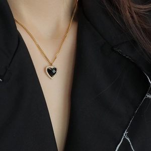 Close-up of a black heart pendant with a sparkling diamond border on a gold necklace chain
