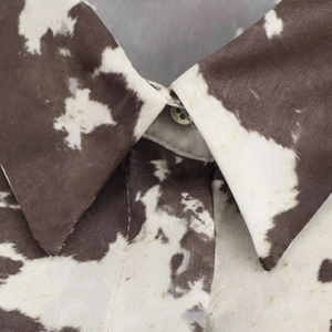 Détail d'un col de chemise pointu avec imprimé vache marron et blanc en tissu soyeux