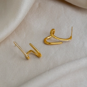 Detailed view of C-shaped gold earrings with paved white zircons on silk background