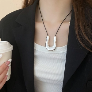 Detail of silver shell-shaped pendant on black rope chain worn by a model in a suit