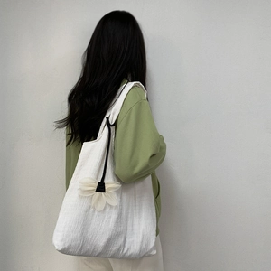 Detail of white pleated canvas tote bag featuring a 3D floral charm on a model's shoulder
