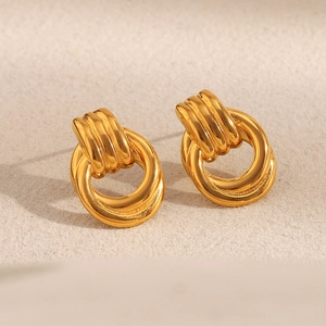 Detail of 18K gold-plated braided circle stud earrings on a textured beige surface