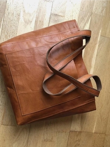Vue de dessus d'un cabas en cuir marron avec poches et anses en tissu sur parquet