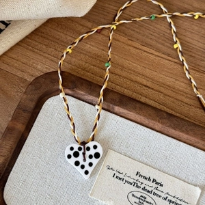 Detail of handmade woven necklace with heart pendant and colorful beads on a wooden tray