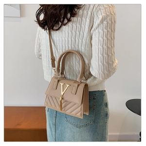 Close-up of beige quilted crossbody bag with golden V-buckle and tassel detail on strap