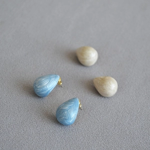 Macro detail of tear-drop enamel stud earrings with blue and beige marble texture