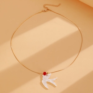 Gros plan du pendentif hirondelle dorée avec incrustation blanche et perle rouge