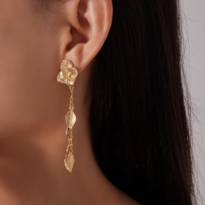 Close-up of elegant gold flower and leaf tassel earrings worn on a model's ear