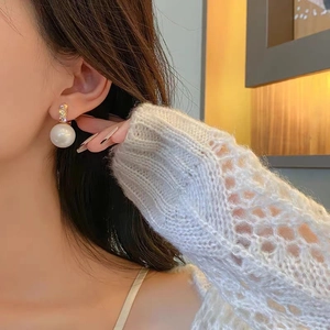 Close-up of pearl stud earrings with sparkling pavé zircons worn by a model