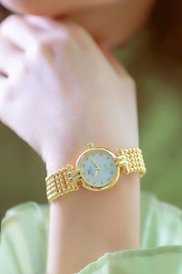 Close-up of gold beaded metal watch strap and white dial with diamond markers