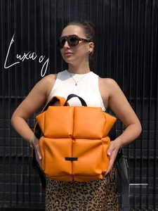 Détail d'un sac à dos matelassé orange vif en éco-cuir tenu par un mannequin