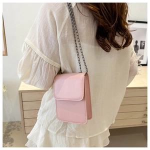 Pink minimalist crossbody phone bag with metal chain strap shown in a cozy home setting