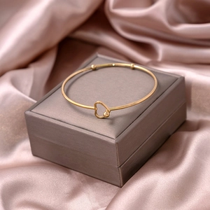 Detail of a thin gold heart-shaped bangle on gray jewelry box and pink silk fabric