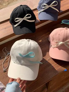 Row of baseball caps with ribbon bows in white, pink, black, and blue on a windowsill