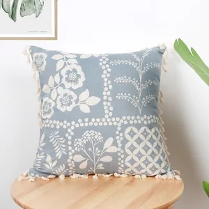 Blue floral cushion cover with white botanical prints and tassel edges on wood stool