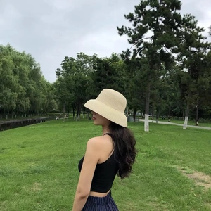 Detail of a beige woven straw sun hat with a rounded brim in a park setting