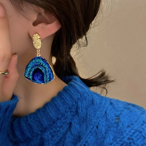 Close-up of blue and green gradient fan-shaped earrings worn by a model in soft lighting