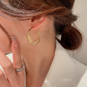 Close-up of golden twist hoop earrings featuring a contrast of matte and polished textures