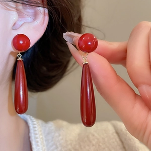 Detail view of elegant dark red drop earrings with gold hooks and smooth glossy finish