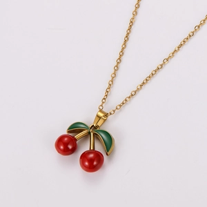 Detail of gold necklace with red cherry pendants and green leaves on white background