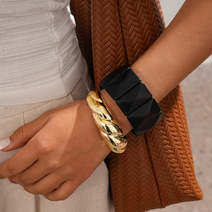 Detail shot of a twisted gold cuff and black geometric square bracelet set on a wrist