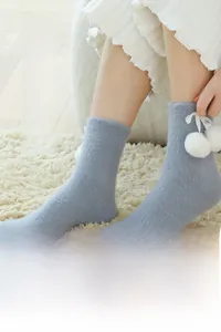 Close-up of light blue fluffy winter socks with white ribbon bows and plush pom-poms