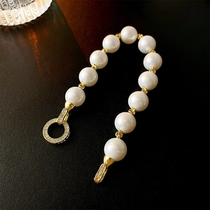 Macro detail of pearl bracelet with gold zircon ring clasp on dark textured leather background