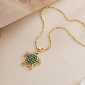 Close-up of 18K gold plated turtle pendant with green gems and zircon detailing