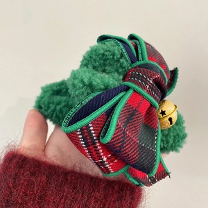 Detail shot of green plush Christmas hair claw clip with plaid bow and small golden bell