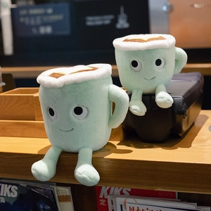 Creative plush latte coffee cup toys with cute smiling faces and dangling limbs on wood
